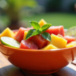 Salada Tropical com Frutas pronta, decorada com hortelã e limão, perfeita para um dia ensolarado.
