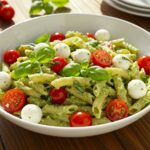 Delicious Light and Creamy Pesto Caprese Pasta Salad served with fresh ingredients like basil, tomatoes, and mozzarella, perfect for any gathering.