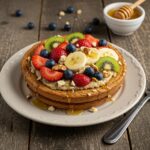 Deliciously presented Baked Protein Pancake Bowl topped with fruits and honey, ideal for a nutritious breakfast, on a rustic wooden table.