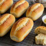 Golden brown crusty chewy French bread rolls on a wire rack, showcasing the final delicious product of homemade bread baking.