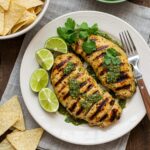 Final presentation of Grilled Salsa Verde Pepper Jack Chicken garnished with cilantro, lime wedges, and tortilla chips, perfect for a flavorful meal.