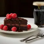 Serving a slice of rich and moist Guinness Chocolate Cake with fresh raspberries and chocolate sauce.