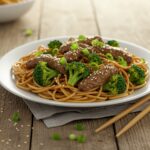 Delicious homemade beef and broccoli lo mein garnished with sesame seeds and green onions, ready to serve.