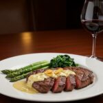 A stunning presentation of juicy steak with creamy garlic sauce, served with vegetables and wine, ideal for a gourmet dinner experience.