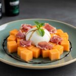 Final presentation of a melon-burrata-prosciutto salad, elegantly plated with colorful ingredients and a touch of balsamic glaze.