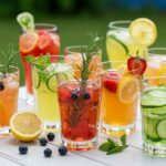 Assorted summer detox drinks displayed on a table with vibrant colors of fruits and herbs under the sun, perfect for hydration.