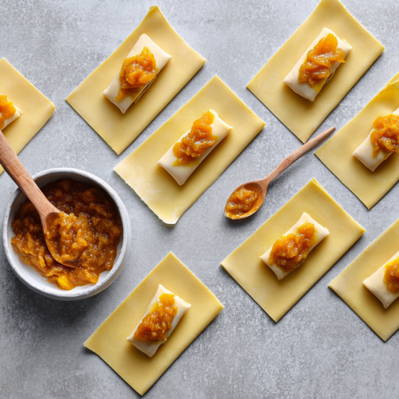 Preparing egg rolls with fresh peach filling on egg roll wrappers in a well-lit kitchen.