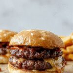 A close-up of a juicy Crack Burger featuring a perfectly toasted bun, melted cheese dripping over a seasoned beef patty, crispy bacon strips, fresh lettuce, tomato slices, and a dollop of sauce, all arranged on a rustic wooden platter.