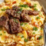 A close-up of a vibrant plate featuring fluffy white rice topped with melted creamy queso sauce, garnished with tender, juicy steak strips, colorful herbs, and a sprinkle of pepper, all arranged attractively on a rustic wooden table.