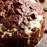A slice of rich, dark chocolate pumpkin bread on a rustic wooden plate, topped with a sprinkle of powdered sugar, showing its moist, dense crumb and swirls of pumpkin and chocolate throughout.