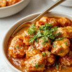 A vibrant plate of butter chicken featuring tender, golden-brown chicken pieces coated in rich, creamy orange sauce, garnished with fresh cilantro and served with steamed rice on a white plate.