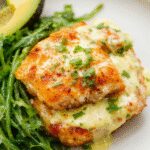 Plates featuring golden-brown salmon balls garnished with fresh herbs, served alongside a vibrant, smooth creamy avocado sauce in a white bowl, with a rustic wooden background and elegant plating