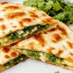 Golden-brown quesadillas sliced open to reveal a melted cheese filling mixed with vibrant green spinach and crumbled white feta cheese, garnished with fresh herbs on a rustic plate.