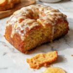 A golden-brown apple cider pound cake sliced to reveal a moist, dense interior, topped with a dusting of powdered sugar and served on a rustic wooden platter, with fresh apple slices and a cinnamon stick garnish, highlighting its fall-inspired flavors.