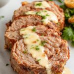 A perfectly cooked pork tenderloin sliced to reveal a juicy, tender interior, coated with a glossy, creamy Dijon sauce, garnished with fresh herbs on a white plate. The dish is presented against a rustic wooden background with a side of colorful roasted vegetables.