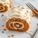 A beautifully sliced pumpkin spice roll cake displaying its creamy swirled filling and moist pumpkin sponge, garnished with a light dusting of powdered sugar, on a rustic wooden platter with autumn leaves around.