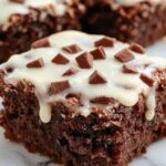 A slice of rich, moist German chocolate poke cake with a glossy chocolate topping, topped with shredded coconut and chopped nuts, served on a white plate with a fork, showcasing the creamy filling and textured topping.