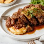 A hearty Italian pot roast served in a rustic ceramic dish, featuring tender chunks of beef coated in rich, dark gravy with visible herbs and vegetables; accompanied by golden-brown oven-baked Gorgonzola polenta slices, topped with a sprinkle of fresh herbs, all presented on a wooden table with a cozy, warm atmosphere.