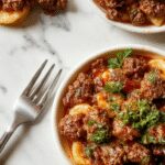 A rustic ceramic bowl filled with savory ground beef and orzo pasta, topped with fresh herbs and a sprinkle of grated cheese. The dish is served steaming hot on a wooden table with a spoon resting beside it, showcasing its creamy, well-seasoned texture and vibrant colors.
