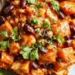 A vibrant skillet dish featuring diced roasted sweet potatoes, black beans, and colorful bell peppers, garnished with fresh cilantro and a squeeze of lime, served on a rustic wooden surface with a sprinkle of cheese on top.