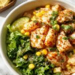 A vibrant street corn chicken rice bowl garnished with fresh cilantro, lime wedges, and a sprinkle of cheese. The bowl showcases grilled chicken, sweet corn kernels, and fluffy rice, arranged appealingly with colorful toppings and fresh herbs.