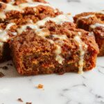 A slices of moist, golden-brown pumpkin bread arranged on a rustic wooden table, accented with a dusting of powdered sugar, fresh pumpkin leaves, and a small bowl of whipped cream. The loaf has a slightly cracked top, revealing a tender crumb inside, enticing and warm.