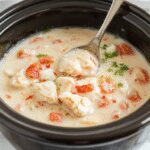 A steaming bowl of white chicken chili garnished with fresh cilantro and a dollop of sour cream, surrounded by ingredients like chicken, beans, and spices. The chili has a creamy texture with visible chunks of chicken and beans, served in a rustic white bowl on a wooden table, with a cozy fall ambiance.